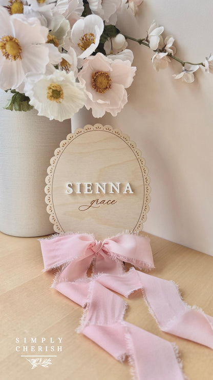 Lace-trimmed sign with raised white SIENNA block lettering and engraved grace